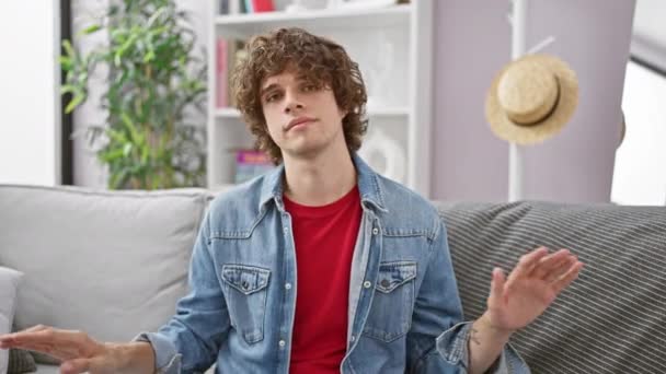 Ein junger Mann gestikuliert nachdrücklich, während er auf einem grauen Sofa in einem modernen Wohnzimmer sitzt.. - Filmmaterial, Video