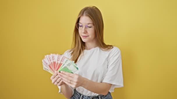 Blonde vrouw onderzoekt Noordse kroon tegen een gele geïsoleerde achtergrond, portretteert financiën en valuta. - Video