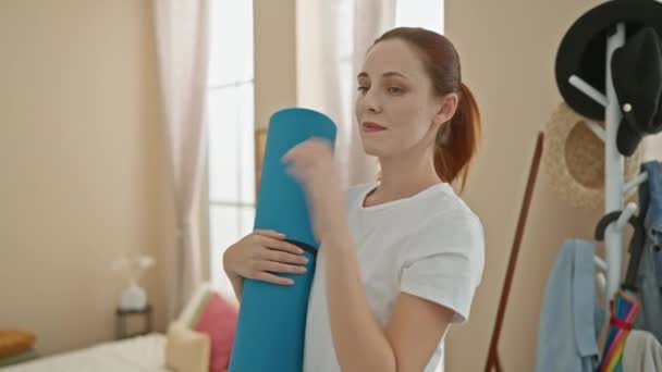 Egy fiatal kaukázusi nő kék jóga matracot tart, és edzésre készül fényes, otthonos nappalijában.. - Felvétel, videó