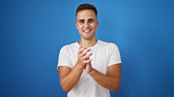 Sonriente hombre guapo aplaudiendo las manos contra un fondo azul aislado, retratando un gesto positivo - Metraje, vídeo