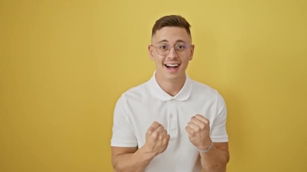 Jubelnder junger hispanischer Mann mit Brille feiert seinen Sieg, schreit aufgeregt mit erhobenen Armen auf gelbem Hintergrund und ist stolz auf seinen Erfolg - Filmmaterial, Video