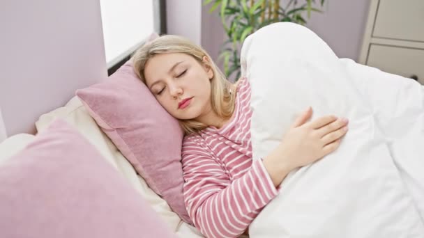 Młoda kobieta w piżamie w paski śpi spokojnie w przytulnej, jasnej sypialni. - Materiał filmowy, wideo