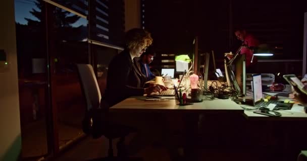 Un grupo de personas enfocadas trabaja intensamente en una oficina poco iluminada, colaborando en un proyecto durante las últimas horas de la noche, reflejando su compromiso y determinación hacia objetivos compartidos.. - Metraje, vídeo