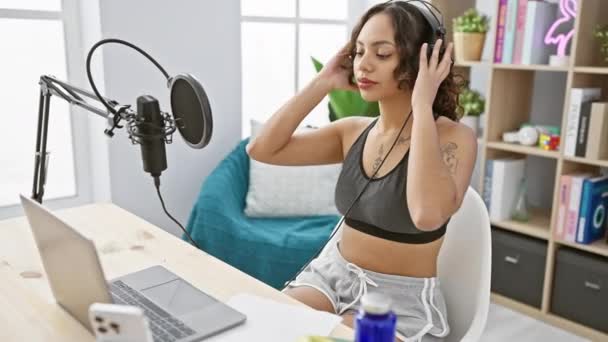Egy mosolygó nő fejhallgatóval felvesz egy podcastot egy otthoni stúdióban, mikrofonnal és laptoppal. - Felvétel, videó