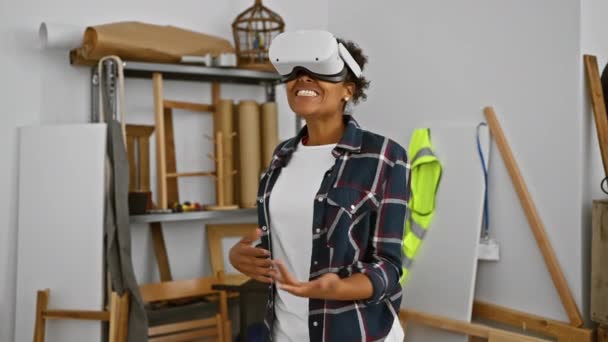 Mujer afroamericana con auriculares de realidad virtual experimentando tecnología en un taller de carpintería. - Metraje, vídeo