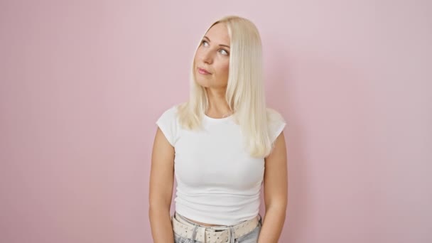 Zelfverzekerde jonge blonde vrouw, serieus kijkend naar de camera, volkomen natuurlijk en eenvoudig stand, over geïsoleerde roze muur. coole levensstijl uitdrukking - Video