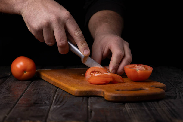 Sebze doğrama. Erkek eller kesme tahtasıyla domates kesiyor. - Fotoğraf, Görsel