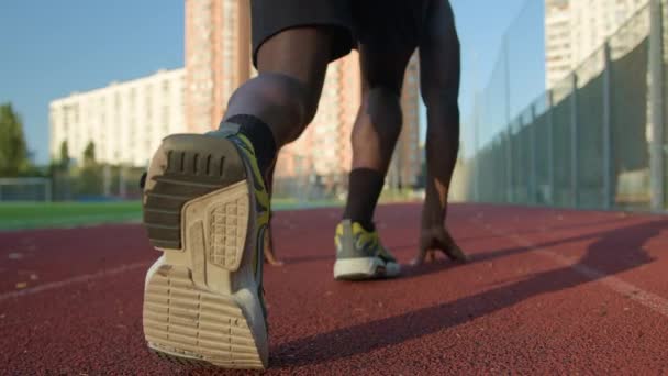 Nízký start pozice zpět pohled běžec Afroameričan chlap chlap sportovec příprava připraven začít na běžecké trati běžec běžec běžec maraton aktivní sportovní trénink venku jogging na město sluneční světlo - Záběry, video