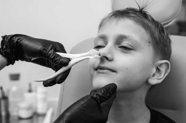 Nasenuntersuchung, kleiner Junge, blonder Teenager lächelnd, in der Praxis des HNO-Arztes sitzend, Nasengänge beim Arzt untersuchend, vertrauensvoll, emotional, lächelnd. - Foto, Bild