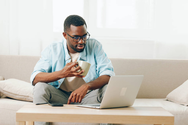 Usmívající se Afroameričan pracující na notebooku a telefonování v útulné domácí kanceláři - Fotografie, Obrázek