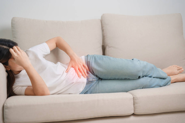 Woman having abdomen pain on the sofa at home. Liver cancer and Tumor, kidney cancer, Jaundice, Viral Hepatitis, Cirrhosis, Failure, Enlarged, Hepatic Encephalopathy, Stomach and health concept - Photo, Image