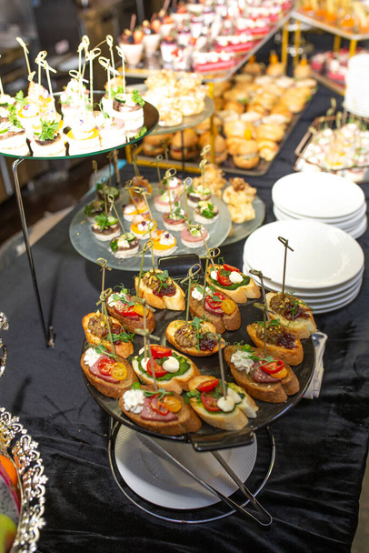 Catering buffettafel met heerlijke hapjes en snacks voor gasten op een feest of bedrijfsevenement. Versierd met zwart tafelkleed en servetten, voedsel visueel geregeld. - Foto, afbeelding