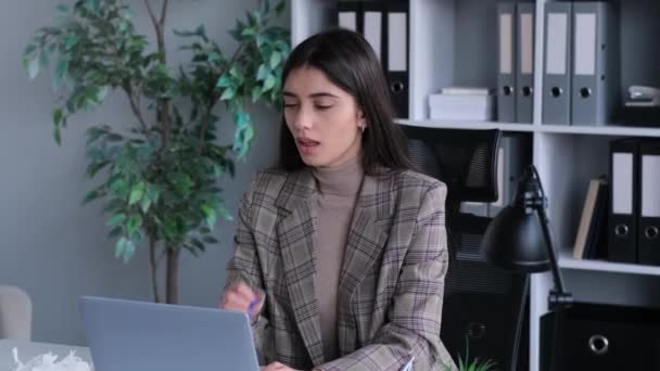Sairas valkoihoinen nuori nainen istuu pöydän ääressä modernissa toimistossa ja työskentelee kannettavan tietokoneen kanssa. Influenssa, keuhkokuume, sairaus, huono terveys käsite. - Materiaali, video