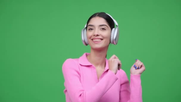 Hymyilevä nuori valkoihoinen nainen kuulokkeissa kuuntelemassa musiikkia, tanssimassa, viettämässä vapaa-aikaa vihreällä taustalla. Audio nautinto, rentoutua mieliala. - Materiaali, video
