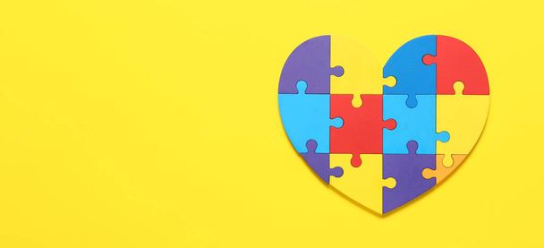 Heart made of colorful puzzle pieces on yellow background. Concept of autism spectrum disorder - Photo, Image