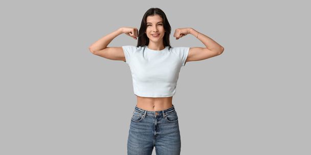 Young woman flexing muscles on grey background. Feminism concept - Foto, Bild