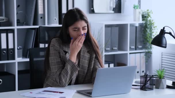 Verveelde blanke vrouw die met een laptop in een kantoor werkt, geeuwt en gestrekt. Het concept van uitputting en vermoeidheid tijdens hard werken. - Video