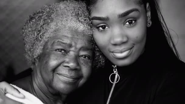 Portret van een zwarte kleindochter met haar bejaarde grootmoeder uit de 80 die de leeftijd van twee generaties in monochroom contrasteert. Portret van Afro-Amerikaanse familieleden in zwart-wit - Video