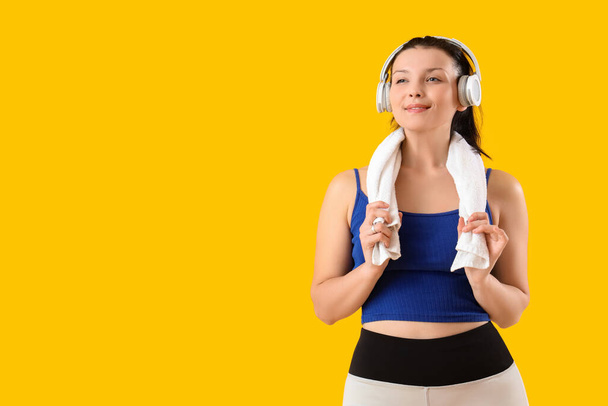 Sportowa młoda kobieta w słuchawkach z ręcznikiem na żółtym tle - Zdjęcie, obraz