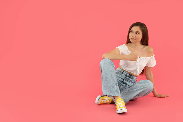 Привлекательная молодая девушка сидит на розовом фоне - Фото, изображение