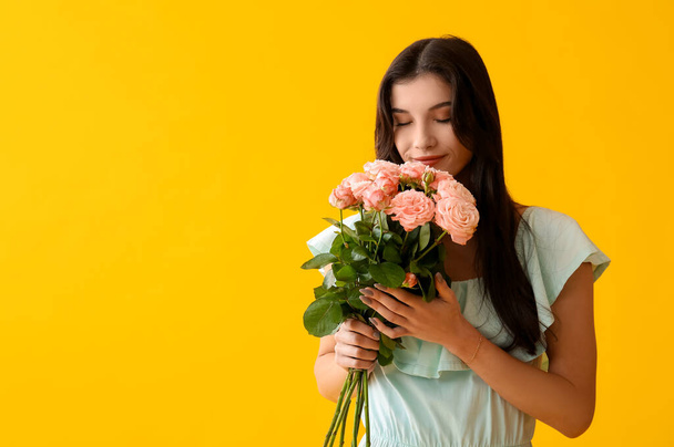 Hermosa joven con ramo de rosas rosadas sobre fondo amarillo. Día Internacional de la Mujer - Foto, Imagen