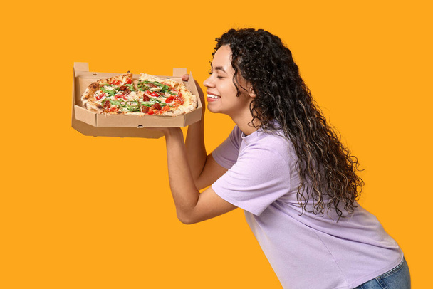 Piękna młoda, szczęśliwa Afroamerykanka z pyszną pizzą na żółtym tle - Zdjęcie, obraz