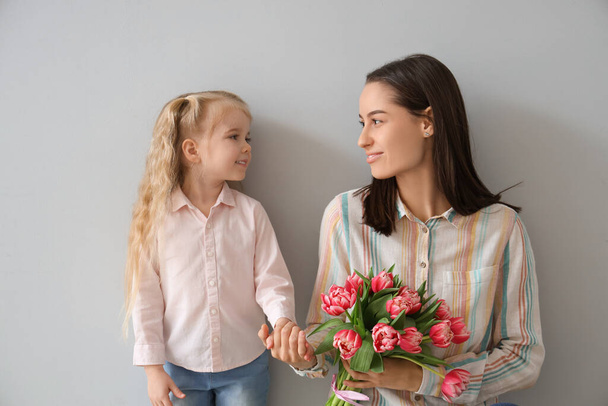 Маленькая девочка поздравляет свою счастливую маму с букетом красивых цветов на сером фоне. Праздник Дня матери - Фото, изображение