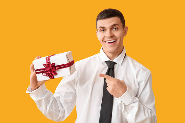 Hombre guapo con caja de regalo sobre fondo amarillo - Foto, Imagen