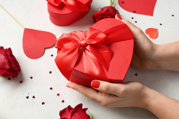 Female hands with red manicure, gift box and decor on white grunge background. Valentine's Day celebration - Photo, Image