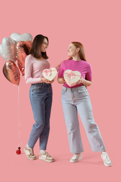 Молодая лесбийская пара с подарочными коробками и шариками на розовом фоне. Празднование Дня Святого Валентина - Фото, изображение