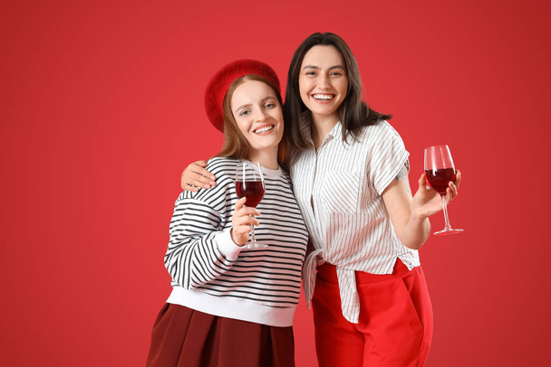 Fiatal leszbikus pár vörös hátterű borral. Valentin-napi ünneplés - Fotó, kép
