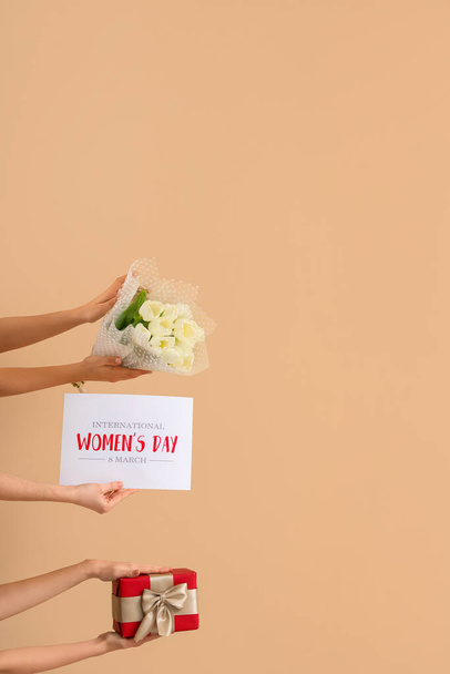 Γυναικεία χέρια με μπουκέτο τουλίπες, κουτί δώρου και εορταστική καρτ ποστάλ σε μπεζ φόντο. Παγκόσμια Ημέρα της Γυναίκας - Φωτογραφία, εικόνα