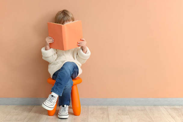 mignon petit garçon lecture livre tandis que assis sur chaise sur fond de couleur - Photo, image