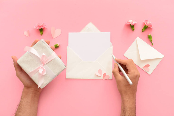 Manos masculinas con sobres, tarjeta en blanco y caja de regalo sobre fondo rosa. Celebración del Día Internacional de la Mujer - Foto, Imagen