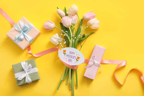 Kaart met tekst HAPPY MOTHER 'S DAY, geschenkdozen en tulpenbloemen op gele achtergrond - Foto, afbeelding