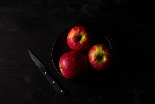 Вид з повітря трьох червоних яблук на тарілці з ножем і темним столом, горизонтальний, з місцем для копіювання - Фото, зображення