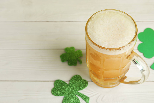 Mug of beer with paper clovers on white wooden background. St. Patrick's Day celebration - Photo, Image