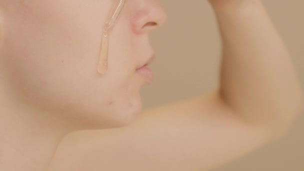 Extreme κοντινό πλάνο του προσώπου Καυκάσια νεαρή γυναίκα βάζει ορό φροντίδας του δέρματος στο μάγουλό της από σταγονόμετρο σε μπεζ φόντο. διαφήμιση ορού φροντίδας δέρματος, αντίγραφο χώρου. - Πλάνα, βίντεο
