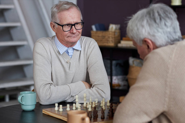 Portrait de deux personnes âgées jouant aux échecs dans la salle commune à la maison de retraite - Photo, image