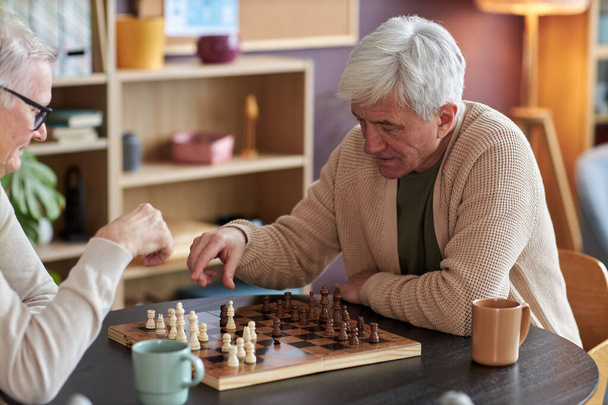 Portré fehér hajú idős férfi sakkozik az asztalnál az idősek otthonában - Fotó, kép
