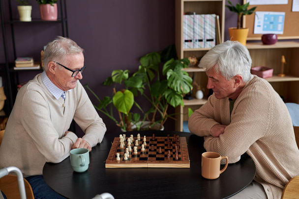 退職後の自宅でテーブルでチェスをする2人の高齢者の側面の肖像画 - 写真・画像