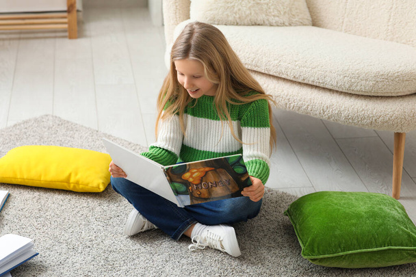家の床に座って本を読んでかわいい女の子 - 写真・画像