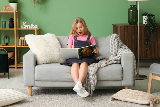 Zszokowana mała dziewczynka czyta książkę na sofie w domu - Zdjęcie, obraz