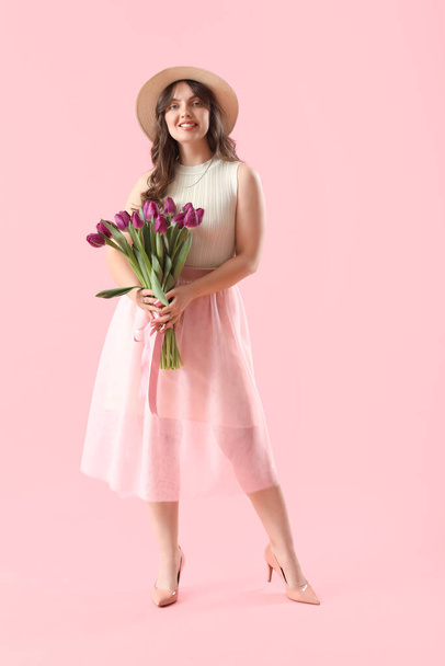 Ευτυχισμένη νεαρή γυναίκα με μπουκέτο από όμορφες μωβ τουλίπες σε ροζ φόντο - Φωτογραφία, εικόνα