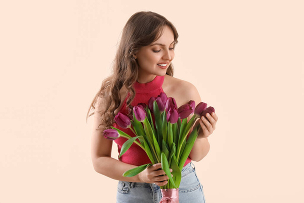 Hezká mladá žena s kyticí krásných fialových tulipánů na béžovém pozadí - Fotografie, Obrázek