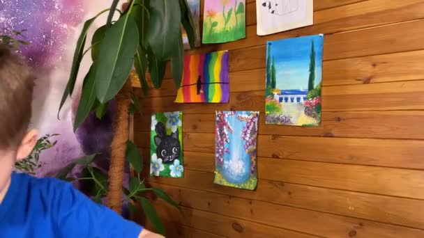 Jeugdige artistieke verbeelding, kinderhobby. Een schattig jongetje drukt zijn creativiteit uit door vrolijk te tekenen met kleurpotloden omringd door artistieke benodigdheden, grillige foto 's, binnenplanten - Video