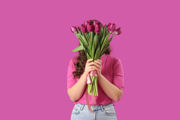 Молодая женщина с букетом красивых тюльпанов на фиолетовом фоне - Фото, изображение