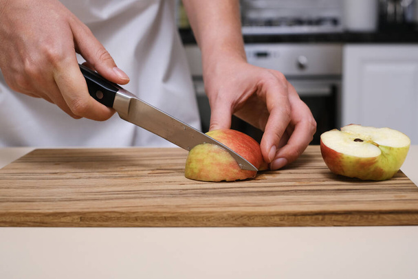 female cook slices an apple on a wooden board in her kitchen - Photo, Image