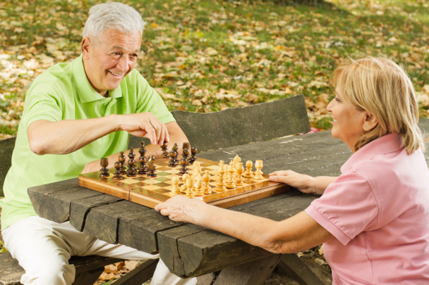 Heureux couple d'aînés jouant aux échecs sur un banc de parc
 - Photo, image