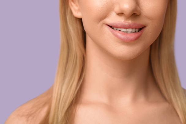 Χαμογελαστή νεαρή γυναίκα με όμορφα χείλη σε λιλά φόντο, κοντινό πλάνο - Φωτογραφία, εικόνα